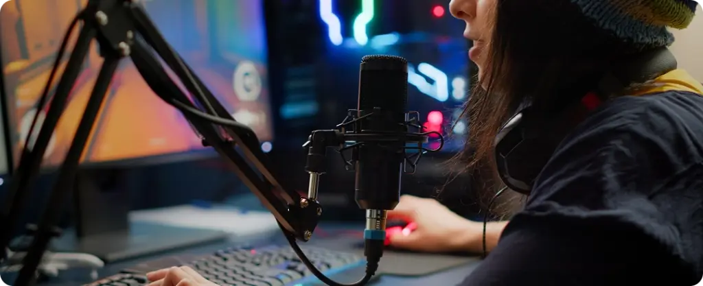 Iemand met een muts op is aan het streamen achter een bureau met een microfoon, toetsenbord en gamingmonitor. De opstelling straalt concentratie en een technologisch geavanceerde sfeer uit