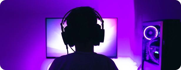 Een kind in silhouet, met een koptelefoon op, zit voor een verlicht computerscherm, terwijl de gaming-setup paars licht uitstraalt, wat een meeslepende, futuristische sfeer creëert