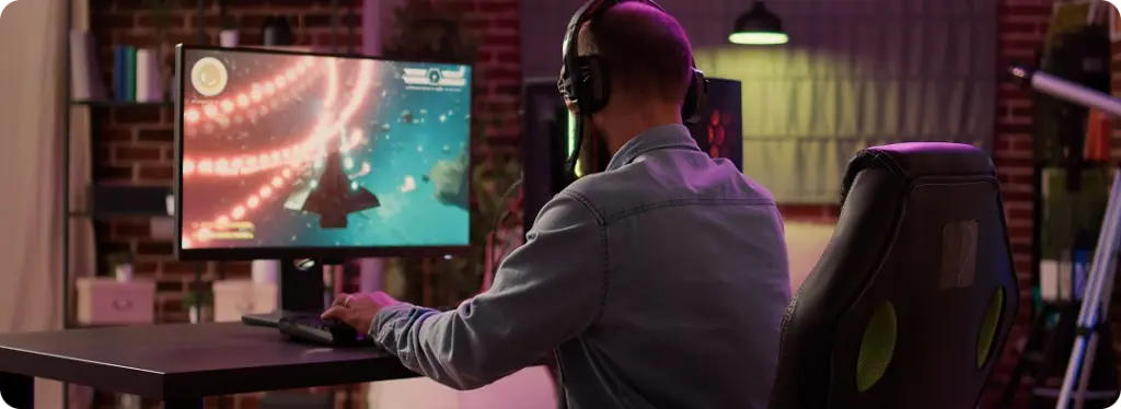 Iemand zit in een gamingstoel, met een koptelefoon op, en is volledig in beslag genomen door een computerscherm waarop een levendig videospel met een ruimtethema te zien is. De kamer is gezellig, met gedempte verlichting